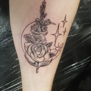 Tattoo of a rose bouquet inside a circular frame, with a slender stem and small star-like sparkles nearby