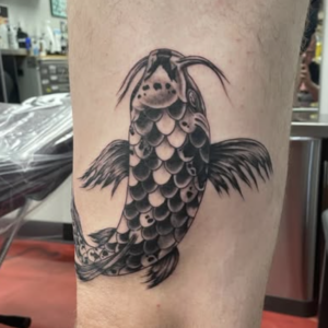 Black and gray koi fish tattoo on a calf with detailed scaled body and flowing fins.