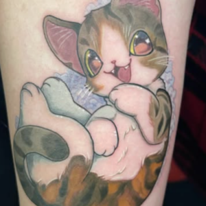 Cute cartoon kitten tattoo lying on its back with big orange and brown eyes, pink nose, and paws raised, on a blue background leg sleeve