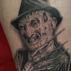 Tattoo of Freddy Krueger from Nightmare on Elm Street on an arm, showing his burned face, fedora, and clawed glove with blades.
