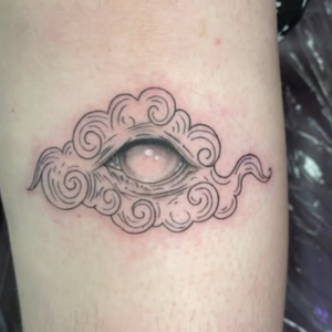 Tattoo of an open eye set in a swirling, cloud-like design on a forearm.