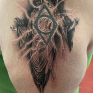 Upper arm tattoo featuring the Deathly Hallows symbol (triangle with circle) and a robed wizard behind it in black and gray shading.